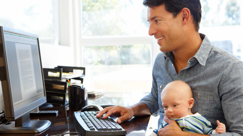 Man working with baby in arms.  This is of course much better for the health of the population. Employees get to spend more family time and enjoy greater flexibility to balance work with life. 
